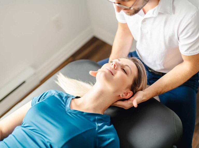 Chiropractor assessing a young athlete’s leg on a treatment table in a clinical setting.